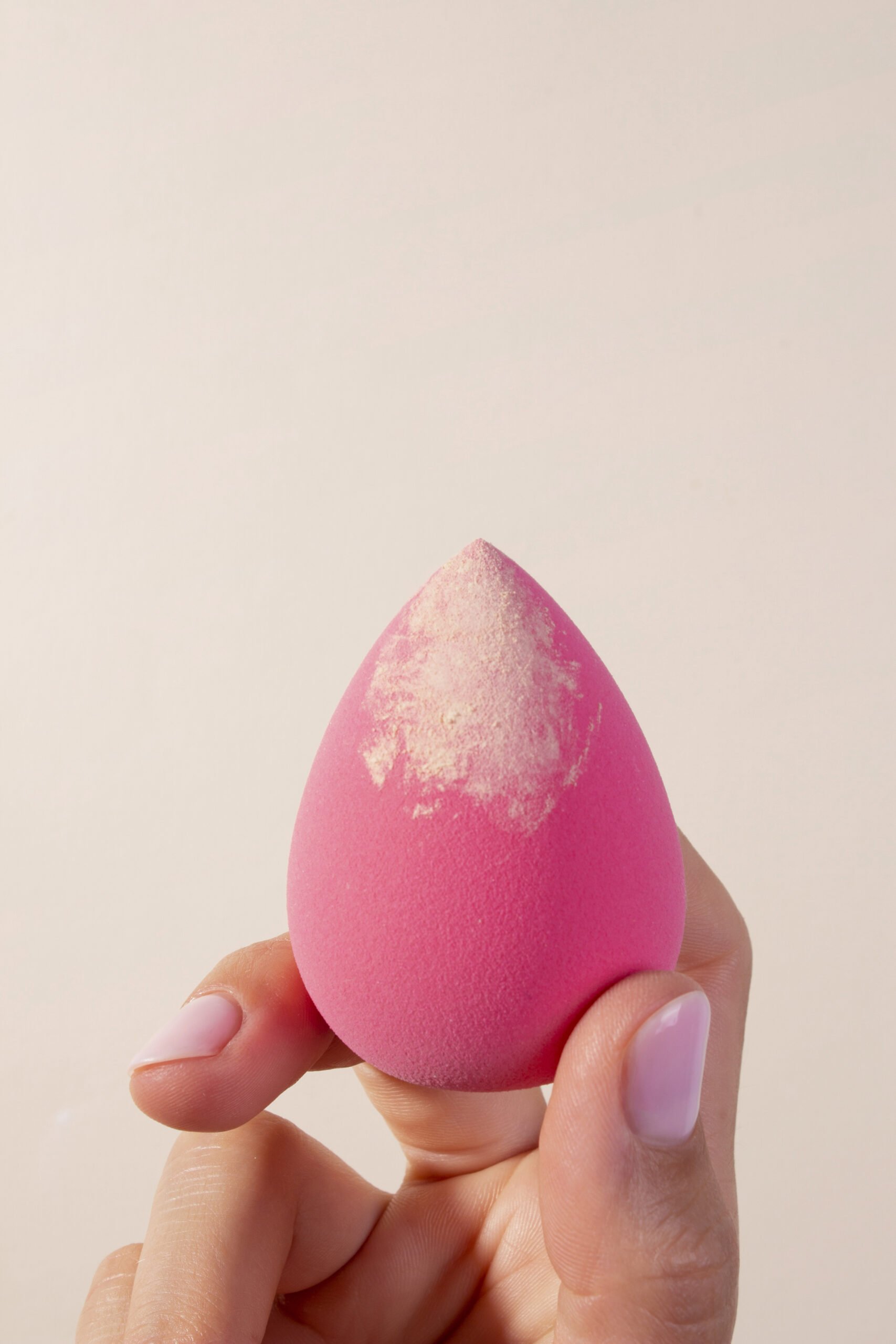 hand-holding-pink-beauty-blender-with-foundation
